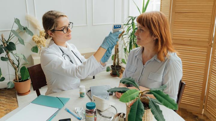 A woman receives a blood pressure check from a doctor in a clinical setting, focusing on health and wellness.