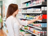  A woman examines a shelf filled with various medicine bottles in a well-lit pharmacy setting.