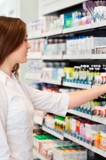  A woman examines a shelf filled with various medicine bottles in a well-lit pharmacy setting.