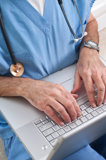 A man in scrubs focused on typing on a laptop, showcasing a professional healthcare environment.