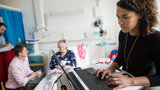 A woman using a laptop in a hospital room, illustrating the intersection of patient care and digital connectivity.