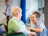 A nurse engages in conversation with an elderly woman seated in a wheelchair, providing care and companionship.