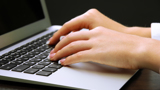 Close-up of hands typing on a laptop keyboard with a dark background. The person appears to have well-manicured nails, and the laptop is silver.