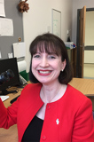 A woman in red, is smiling while holding a camera